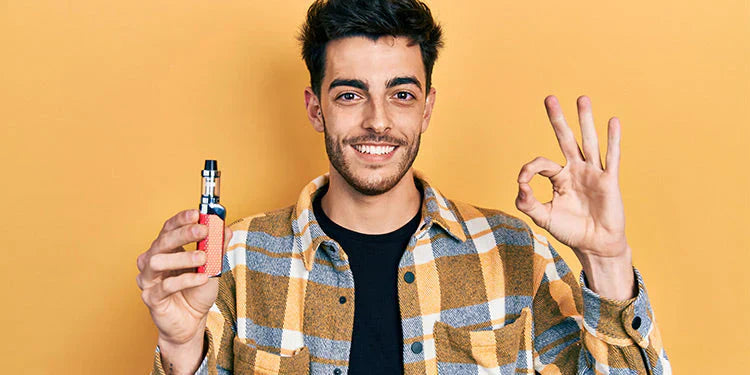 A person holding a vape device and making an "OK" hand gesture against a yellow background.