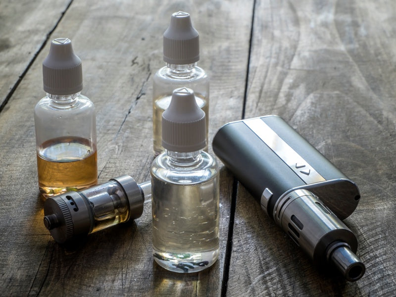 Vape mod, tank, and three bottles of e-liquid on a rustic wooden table.