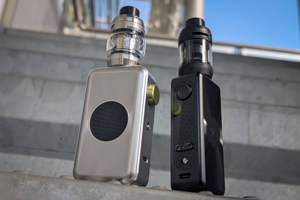 A silver and a black Vaporesso box mod vape, both with tanks, stand on metal stairs.